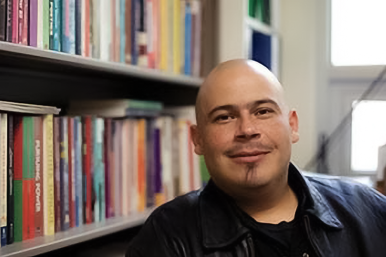 Headshot of Roberto Hernandez posing in front a bookshelf in a room with natural lighting