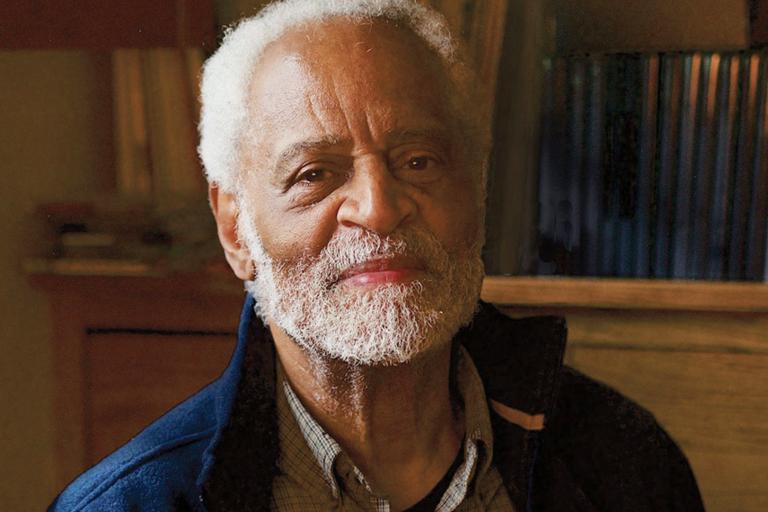 Head shot of Troy Duster, warm-lighting with a bookshelf in the background